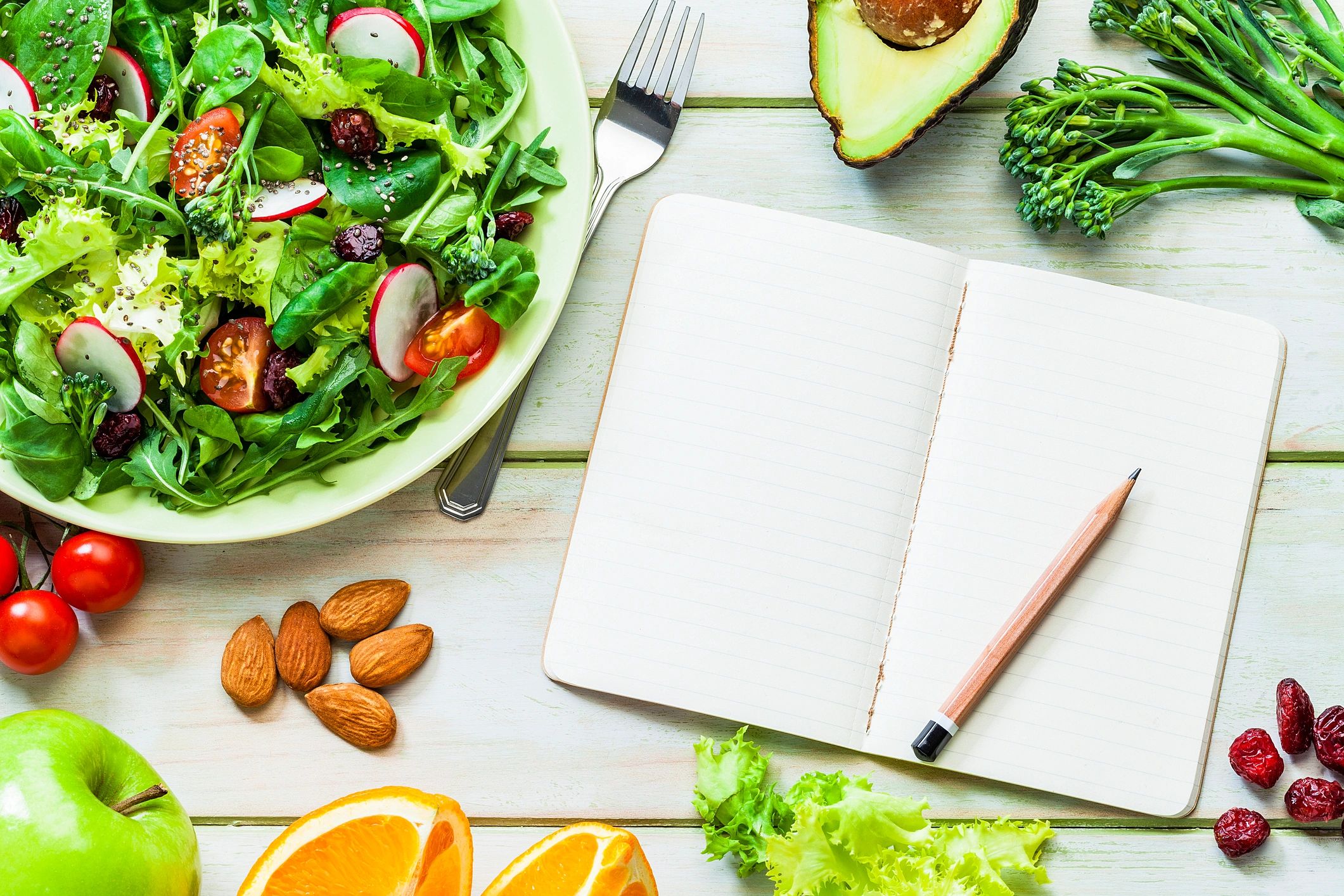 Healthy foods arranged around a blank notepad for meal planning
