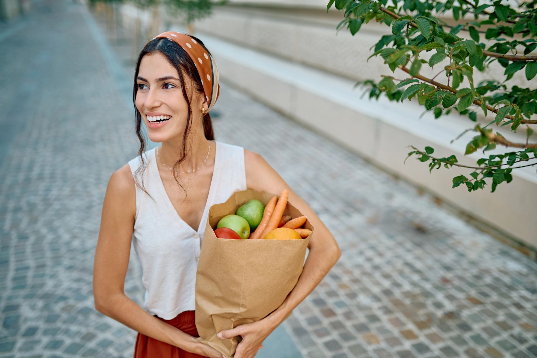 Smiling person carrying groceries in a paper bag while walking in the city